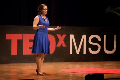 Emily on stage with TEDx MSU logo in background