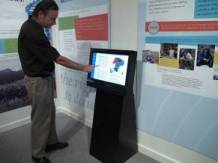 Man standing and touching screen, with informational posters on wall