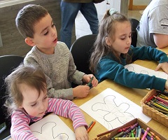 Three children sitting at table with crayons and drawings